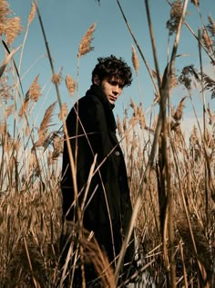 a young man standing in tall grass with his eyes closed and looking at the camera