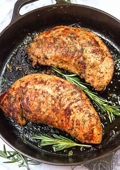 two pork chops cooking in a skillet with rosemary sprigs on the side