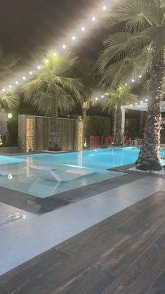 an empty swimming pool with palm trees and lights on the ceiling, in front of a building