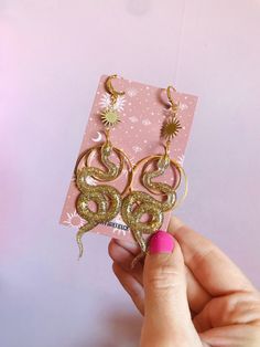 Celestial snake earrings. The earrings are big and will surely catch people's eyes but luckily they weigh next to nothing.  The snake is made out of resin and glitter. All the brass details and hooks are hypoallergenic and goldplated.  The whole earring measures 10 cm/3.9 inches. If you don't hooks you can choose rings or clipons in the menu. Both options are also goldplated and nickelfree. The rings are small closed hoops with about 1 cm/0.4 inches big.  If you would like the snakes in another Gold Snake-shaped Jewelry With Pierced Ears, Gold Snake-shaped Earrings With Pierced Ears, Handmade Gold Snake-shaped Earrings, Gold Snake Jewelry For Pierced Ears, Handmade Gold Snake Earrings, Gold Snake Earrings For Party, Gold Snake-shaped Earrings For Gift, Snake-shaped Earrings With Ear Wire For Gift, Snake-shaped Earrings With Ear Wire As Gift