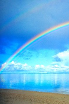 a rainbow appears over the ocean on a sunny day with blue sky and water in the background