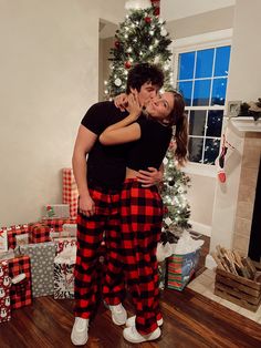 a man and woman hugging in front of a christmas tree with presents on the floor