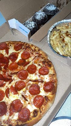 a pepperoni pizza sitting on top of a box next to a plate of pasta