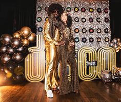 a man and woman standing next to each other in front of a backdrop with disco balls