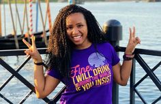 a woman with long hair standing next to a body of water giving the peace sign