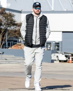 a man walking down the street wearing a black vest and white sneakers with his hands in his pockets