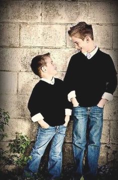 two boys standing next to each other in front of a brick wall