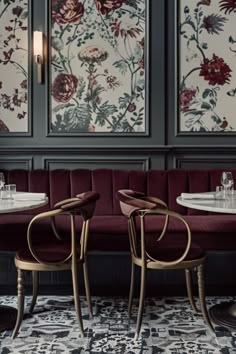 two red velvet chairs sitting next to each other in front of a wall with flowers on it