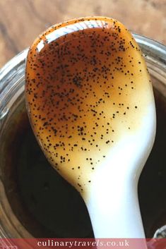 a spoon full of brown liquid with black speckles on it, sitting in a jar