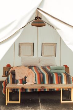 a bed sitting under a tent next to pillows and blankets on top of a wooden bench