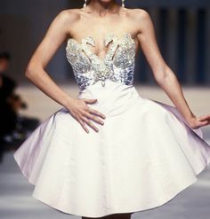 a woman in a short white dress on the runway with her hands behind her back