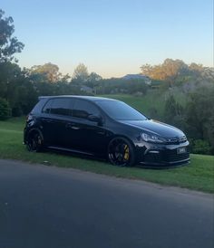 a black car parked on the side of a road next to a lush green field