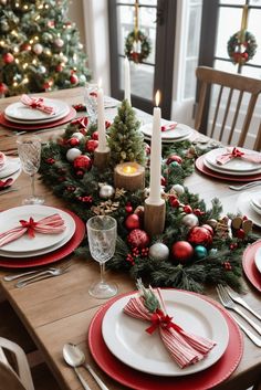 a christmas table setting with red and white plates, silverware and candlesticks