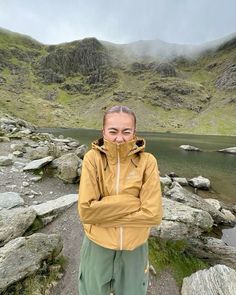 a woman standing on top of a rocky hillside next to a lake