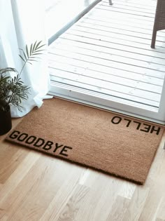 a door mat that says goodbye next to a potted plant on a wooden floor