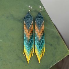 Amazing handmade seed bead earrings with beautiful green-yellow-turquoise-orange design. Emphasize your beauty and personality - be beautiful and brilliant every day! 🔎Size of Earrings with hooks: 15 cm (5.9") long and 2.5 cm (0.98") wide. Beadwork part: 13.2 cm long. I use only high-quality material in creating my works - that's why this thing will please you for a long time and will not cause any trouble in using! This Earrings comes packed in a beautiful box, ready to give as a gift! Earrings are sewed with nylon thread. I wax thread to keep earrings shape as firm and steady as possible. They may occasionally roll up while wearing, as every other beaded items. So you have to flatten them by hands. Lifehack. If you want for earrings to be firm, you can use a hairspray. Flatten an earrin Seed Bead Fringe Earrings, Bead Fringe Earrings, Beadwork Earrings, Boho Earring, Bead Fringe, Yellow Ombre, Jaune Orange, Yellow Turquoise, Orange Design