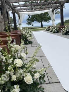 white flowers and greenery are on the ground next to pews at an outdoor ceremony