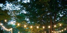 an outdoor dining area is lit up with string lights and tables set for dinner under the trees