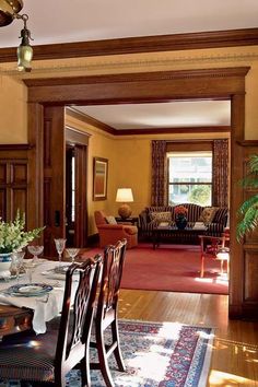 a formal dining room with wood paneled walls and wooden flooring is seen through an open doorway