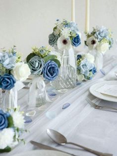 the table is set with blue and white flowers in vases, silverware, and napkins