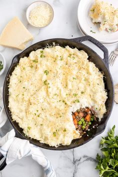 a skillet filled with mashed potatoes and vegetables on top of a marble counter