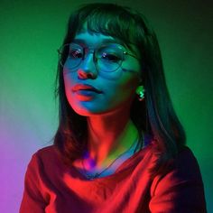 a woman wearing glasses and standing in front of a neon colored background with her hands on her hips