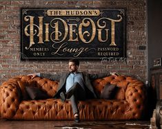 a man sitting on top of a couch in front of a sign that says hudson's hideout lounge