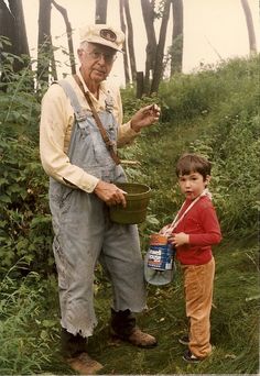 an old man and young boy are standing in the grass with buckets on their shoulders