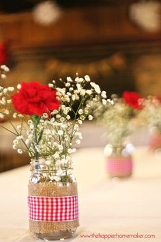 red and white flowers in a mason jar on a table with other vases filled with baby's breath