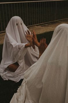 two people dressed in white are sitting on the grass and one is covering his face with her hands