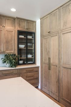 a large kitchen with wooden cabinets and white counter tops in front of a plant on the island