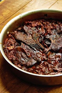 a pot filled with meat and sauce on top of a wooden table