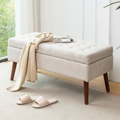 a white bench with a blanket and slippers on it in front of a window