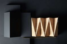 an abstract sculpture made out of plywood on a black surface with two shelves in the background