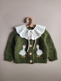 a green sweater with white collar and two ducks on the front, hanging from a wooden hanger