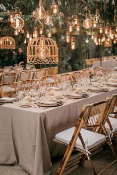 a long table is set up for an outdoor dinner party with hanging lights and birdcages