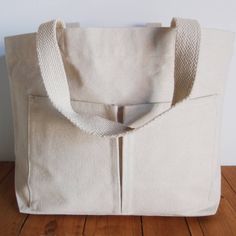 This tote bag has two pockets on outside and a pocket on the inside. It measures 13.5" wide, 13.5" high, and has a bottom gusset that is 2.75" deep. There are two handles for carrying by the shoulder or clutching by hand. The fabric is thick and sturdy. It is made of natural organic cotton. Organic refers to how the cotton is grown. Double Handle Canvas Bag With Pockets For Shopping, Canvas Satchel With Pockets For Shopping, Shopping Canvas Satchel With Pockets, Rectangular Satchel With Pockets For Shopping, Shopping Tote Shoulder Bag With Pockets, Cotton Tote Weekender Bag With Pockets, Rectangular Cotton Weekender Bag With Pockets, Daily Use Tote Satchel With Pockets, Cotton Shoulder Bag With Pockets For Shopping