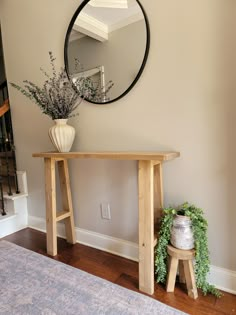 a wooden table with a mirror on the wall above it next to a potted plant