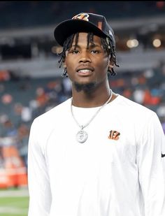 a man with dreadlocks standing in front of a football field wearing a hat