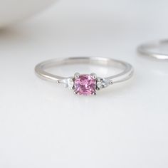 Sweet, simple, and dainty ring. Perfect for a minimalist look, or for stacking. It adds a fun pop of color to your look! Featuring a pink cushion cut stone with pear stones adorning both sides - making this a delicate and beautiful ring!Pink Stones are said to indicate a feeling of rest and peacefulness. It also said that that a person wearing the ring will feel loving, affectionate and happy. Made of 925 Sterling Silver Available in 14k Gold or Rhodium Plating We use a THICK 14k Gold plating - Simple Stone Ring Design, Silver Ring With Pink Stone, Pink And Silver Ring, Simple Stone Ring, Layering Diamond Necklaces, Stone Ring Design, Precious Stones Rings, Pink Cushions, Cushion Ring