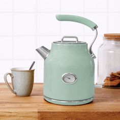 a tea kettle sitting on top of a wooden counter next to a cup and spoon