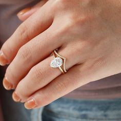 a woman's hand wearing a gold ring with a pear shaped diamond on it