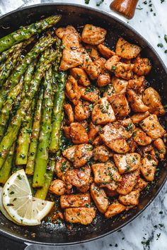 chicken and asparagus in a skillet with lemon wedges