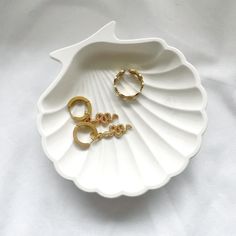 two gold rings sitting on top of a white shell shaped dish with the word love spelled in it