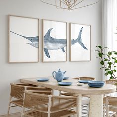 a dining room table with chairs and pictures on the wall above it, along with two blue vases