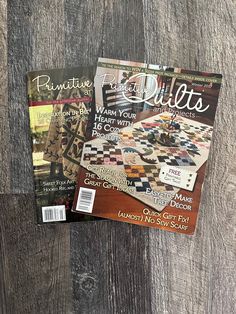 two magazine covers sitting on top of a wooden table next to each other and one has a quilt