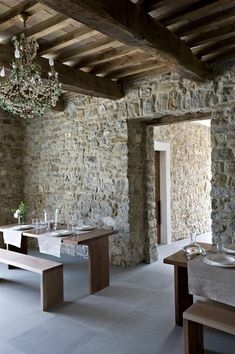 an empty dining room with stone walls and wooden beams, chandelier hanging from the ceiling