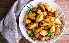 a white bowl filled with cooked potatoes on top of a wooden table next to a gray napkin