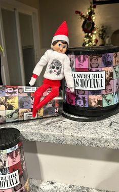 an elf doll sitting on top of a counter next to a canister and christmas tree