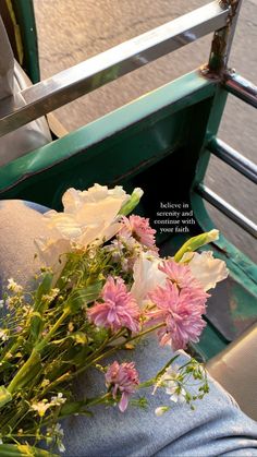 a bouquet of flowers sitting on the back of a green vehicle with someone's legs